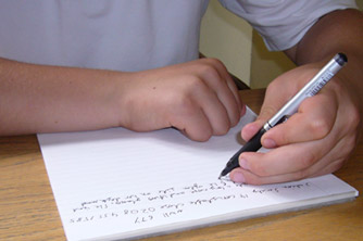 A left-handed child writing on lined paper with a pen.