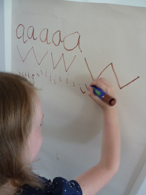 A child writing rows of letters (aaa, wwww, iiii) on a whiteboard