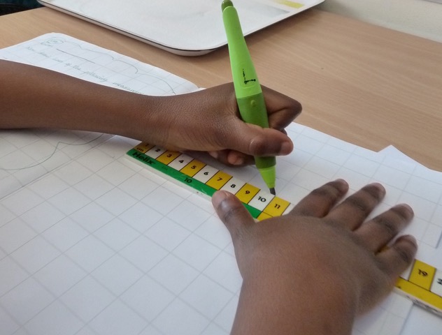 The hands of a child steadying a ruler and drawing a line.
