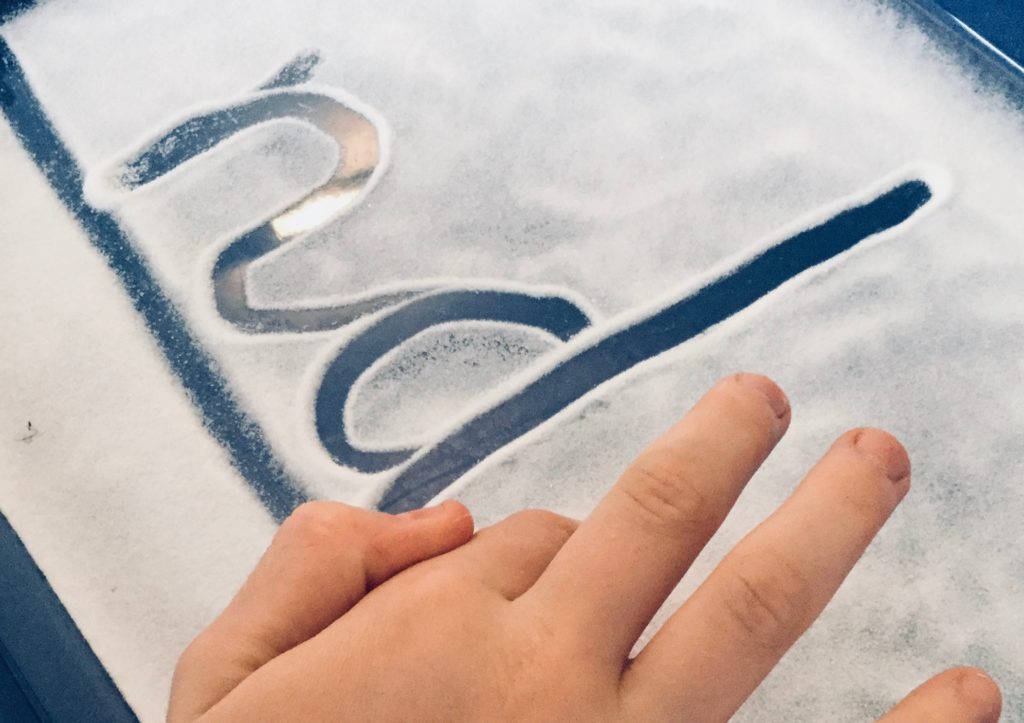 A young child makes letters in sand, showing a join of n to d